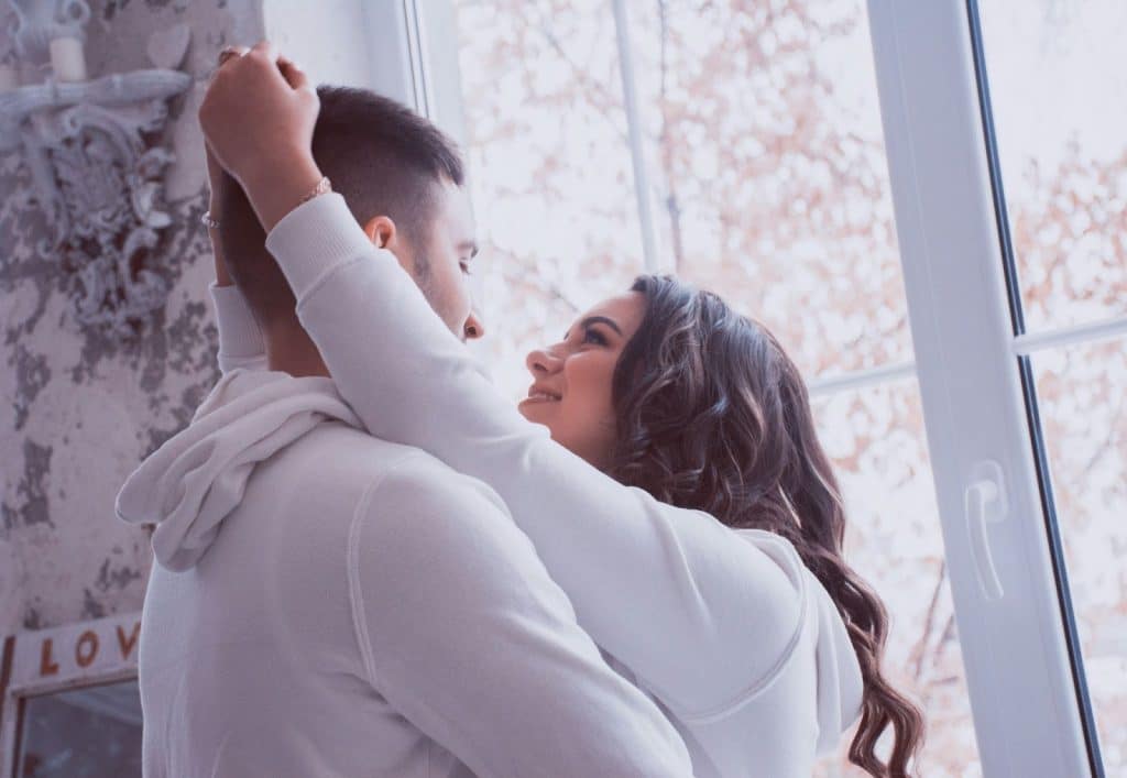 A picture of couple cuddling beside the window.