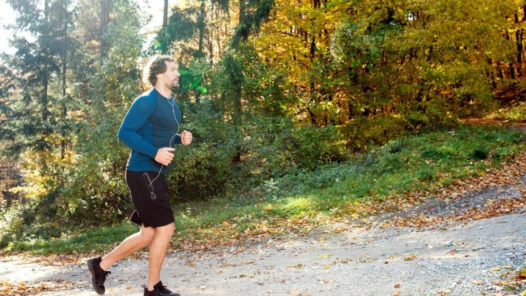 A man jogging on a leaf-strewn trail in the woods.