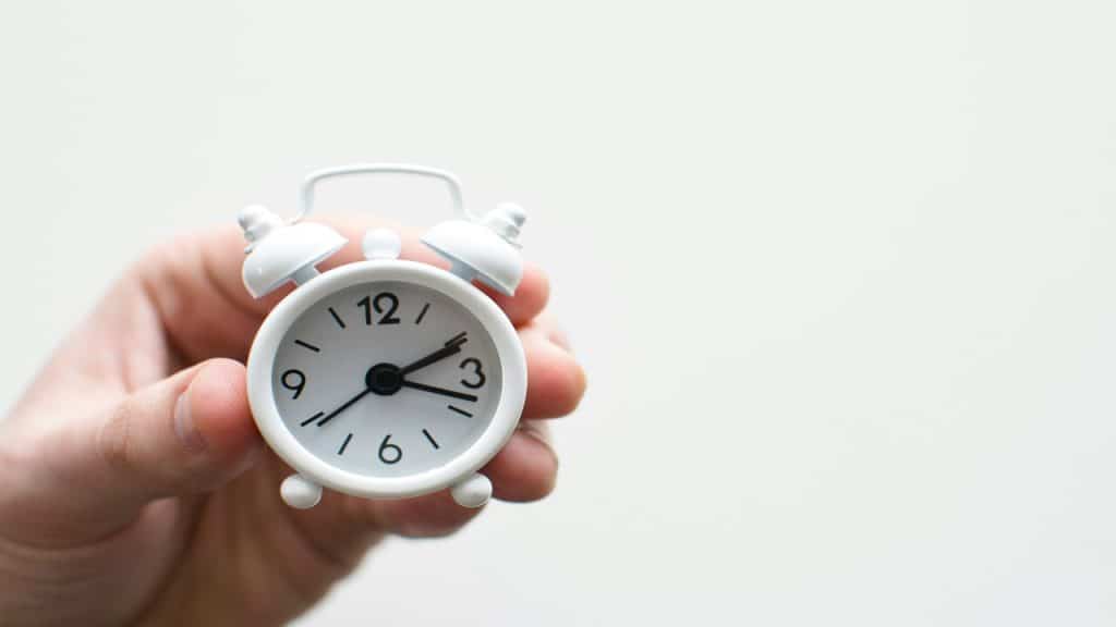 A hand holding a mini alarm clock