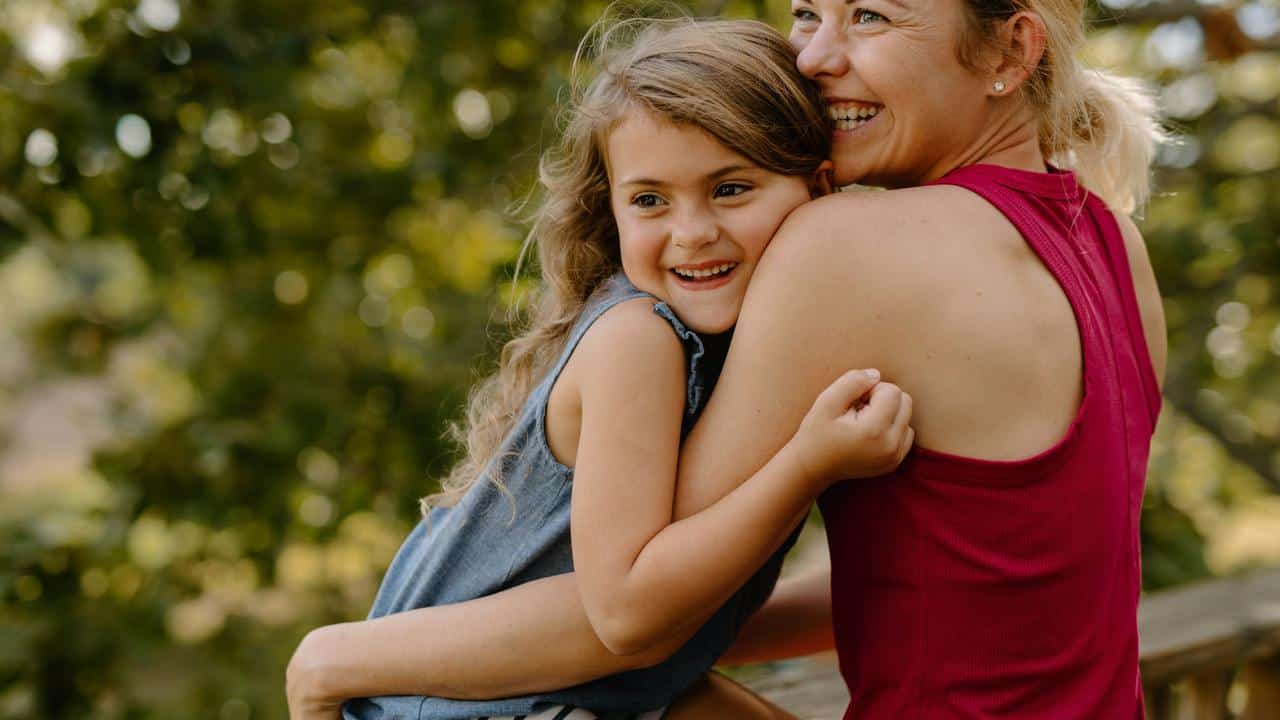 A mother embracing her smiling daughter outdoors.