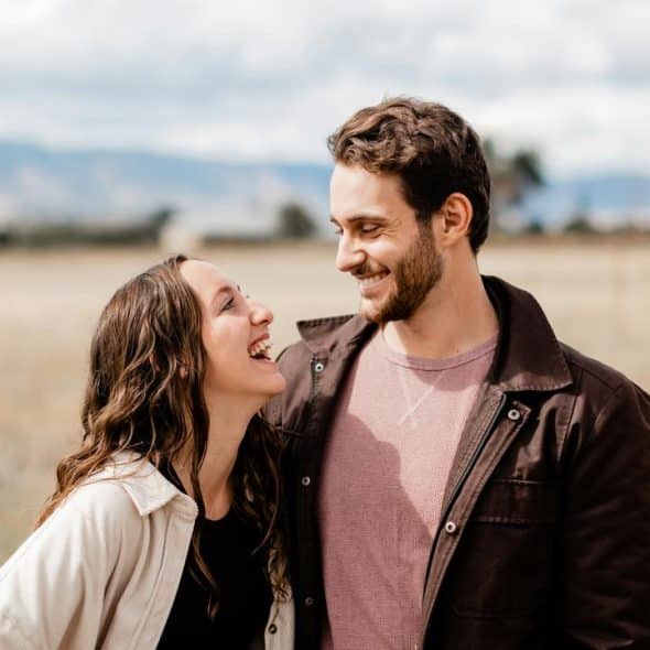 A smiling couple standing in a field looking at each other.