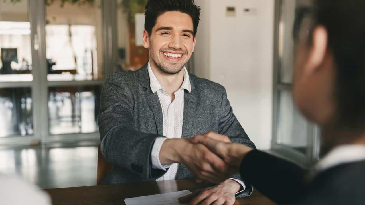 A smiling man shaking hands across a table.