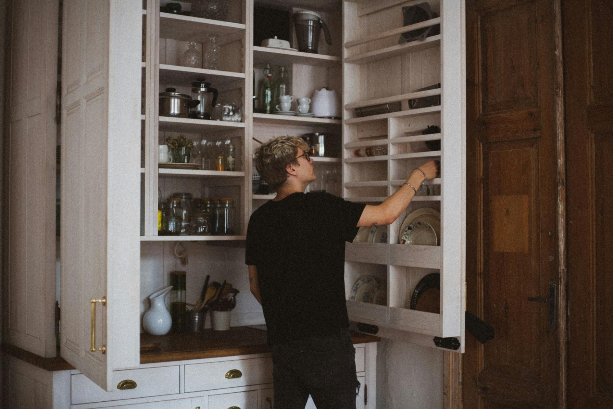 A man organizing a cabinet full of plates.