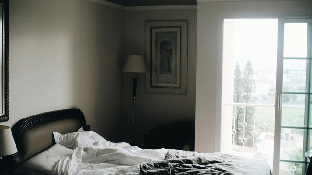 A man lying in bed under a blanket, gazing off in dim light.
