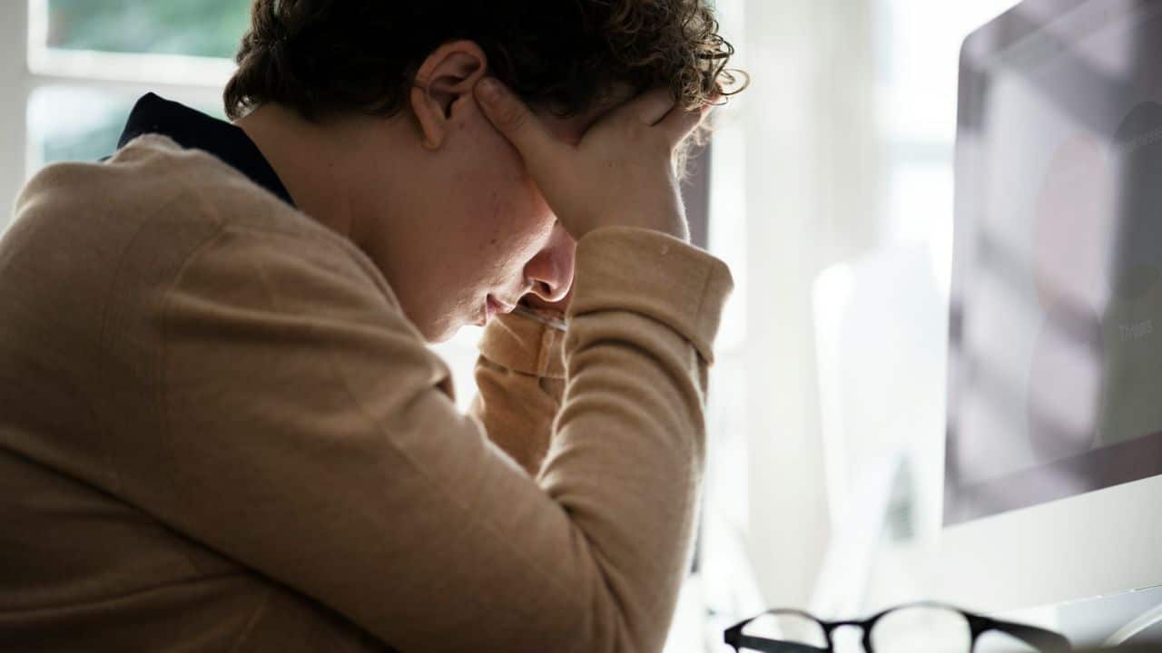 A person with short, curly hair holds their head in their hands, looking distressed.