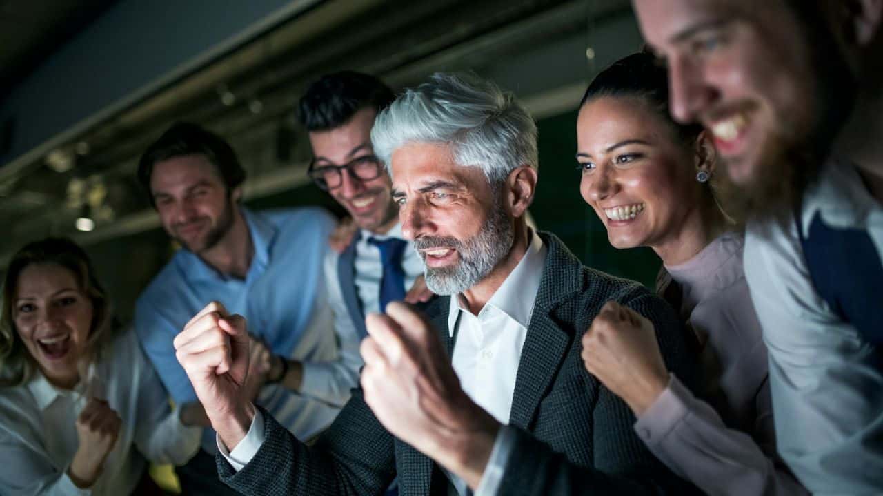 A group of diverse people smile and cheer, celebrating a success together.