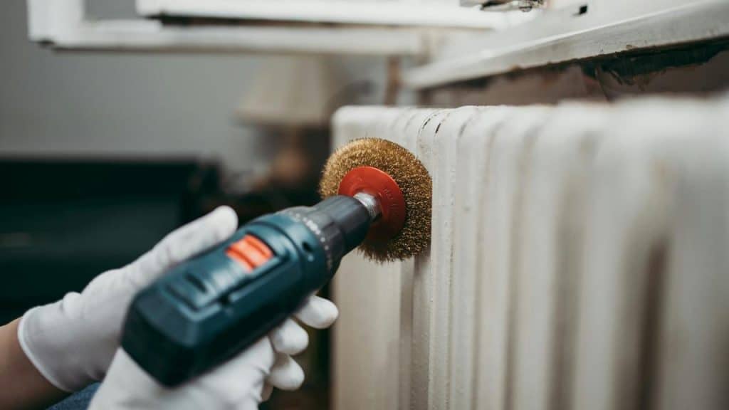 A rotary tool with a wire brush attachment cleaning a radiator surface.