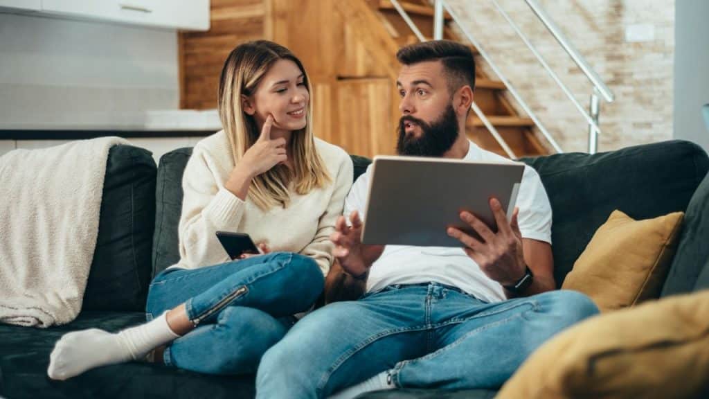 A man and a woman on a couch, he shows her something on a tablet.