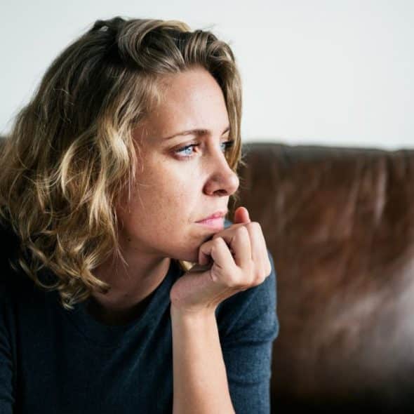 A woman with wavy blonde hair rests her chin on her hand, looking off to the side.