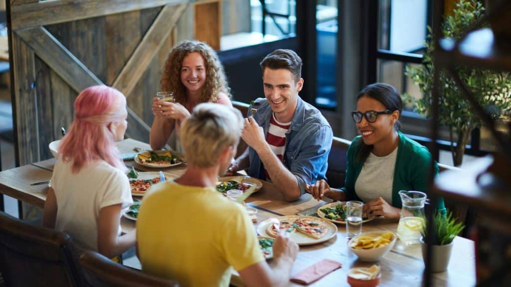 A group of friends sharing pizza and salad at a restaurant table.