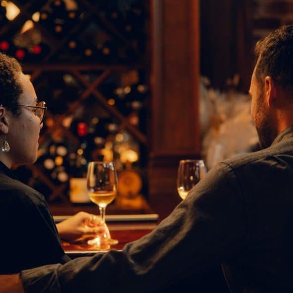 A couple seated at a wine bar holding glasses.
