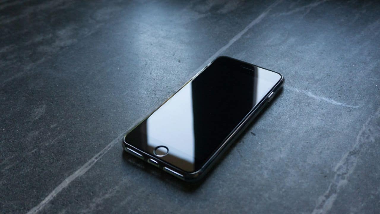 A sleek black smartphone with a reflective screen rests on a dark, patterned surface.