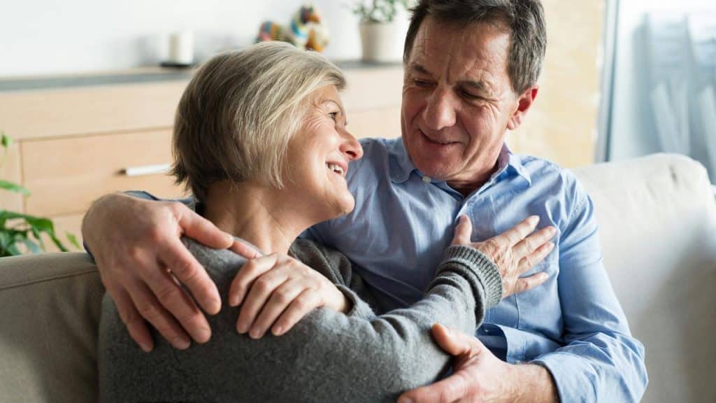 An elderly couple hugging and smiling on a sofa.