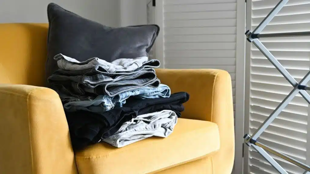 A neat stack of folded clothes rests on a yellow armchair.