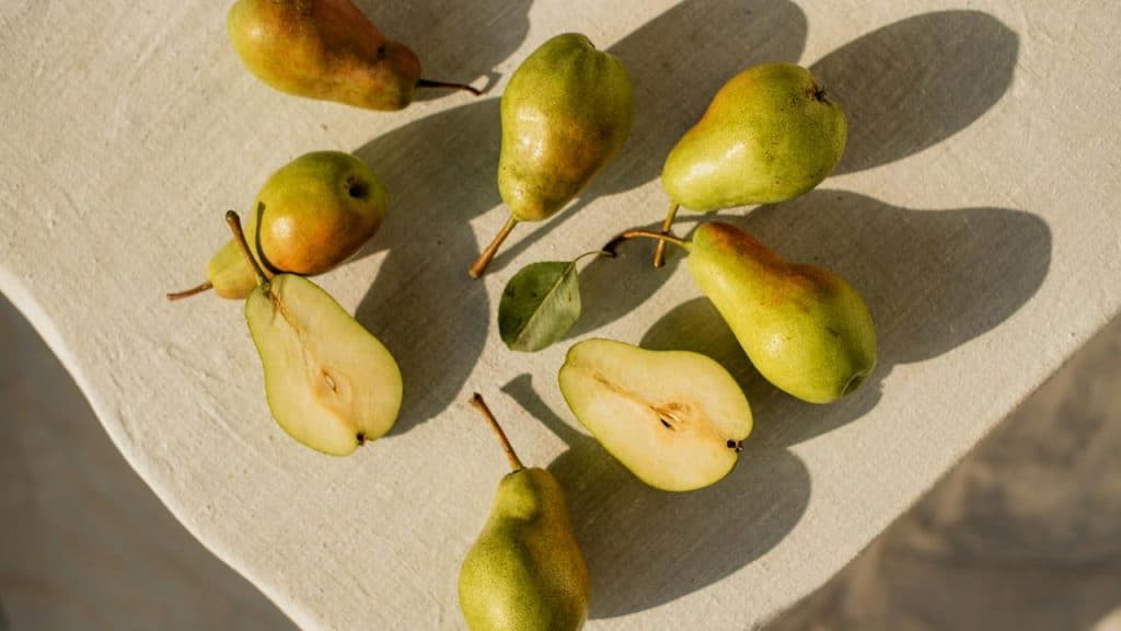 A scatter of green pears, some whole and some halved, on a light cloth surface.