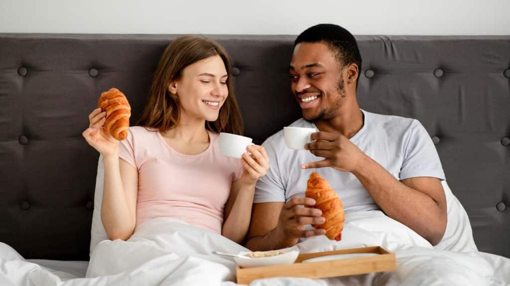 A couple in bed sharing coffee and croissants.