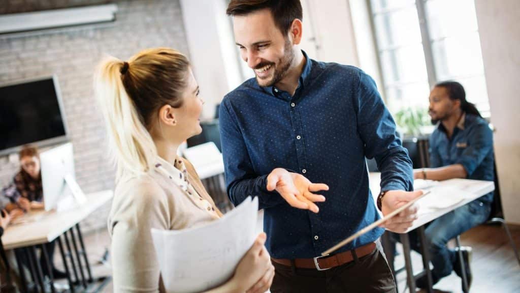 A man and a woman smiling while discussing papers in an office.