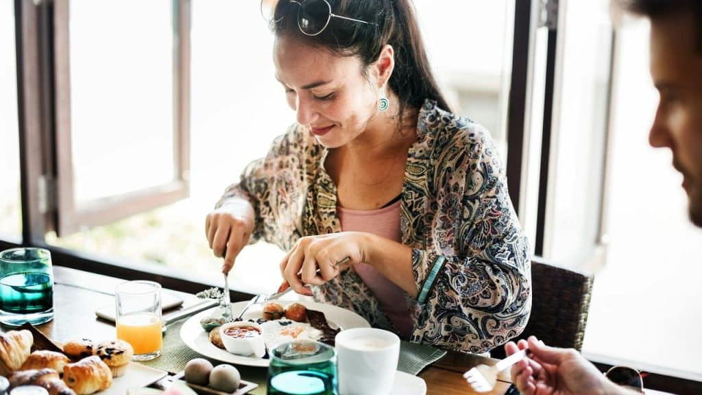 A woman cutting into a breakfast plate at a table.