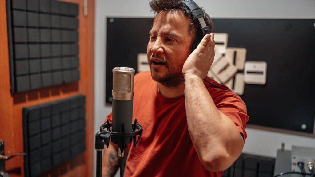 A man wearing headphones singing into a studio microphone.