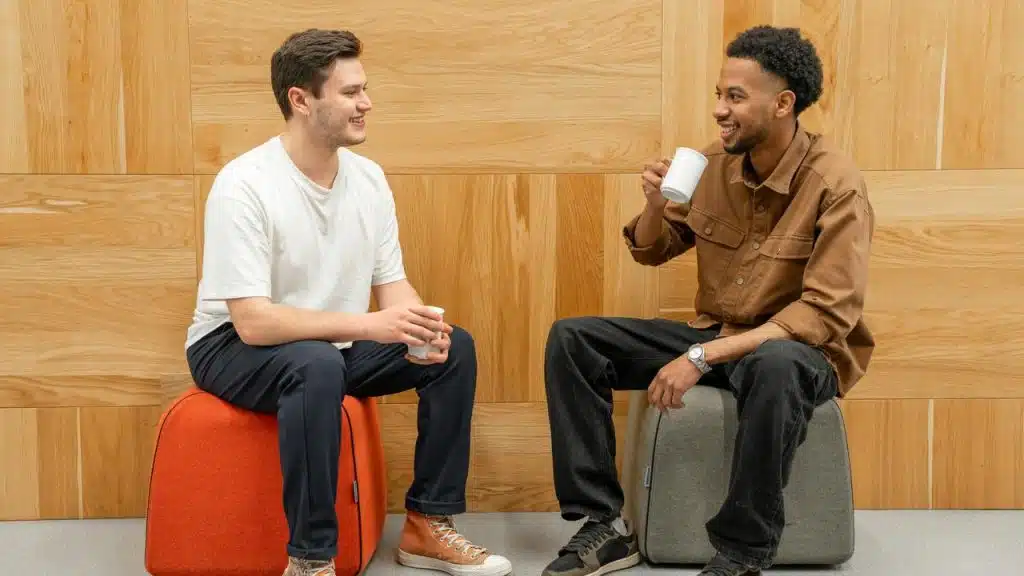 A pair of men seated on stools, drinking coffee and chatting.