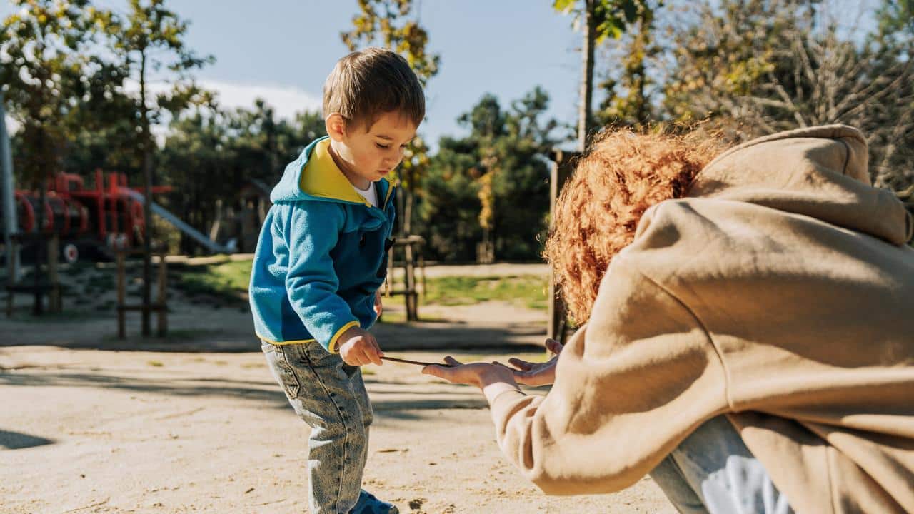 A child handing a stick to an adult at a park.