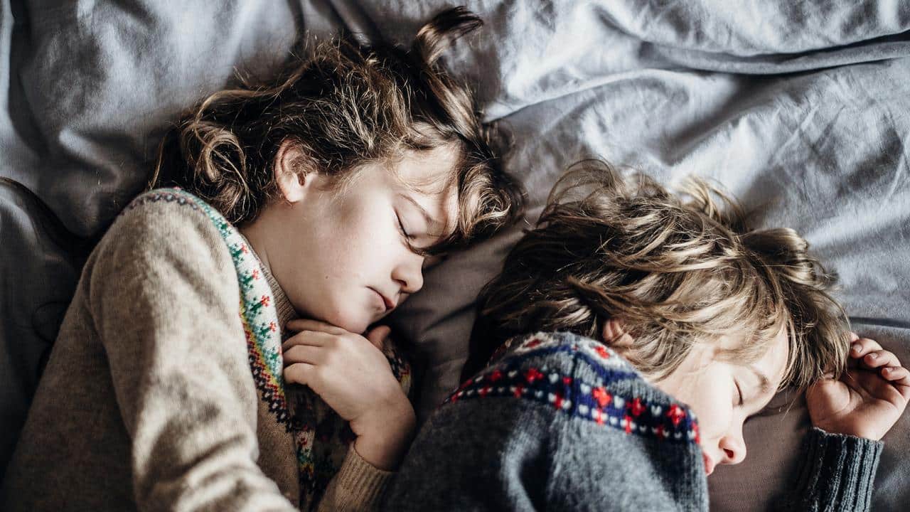 A pair of children sleeping side by side on a bed.