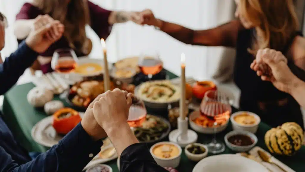 A group holding hands around a table set with food and candles.