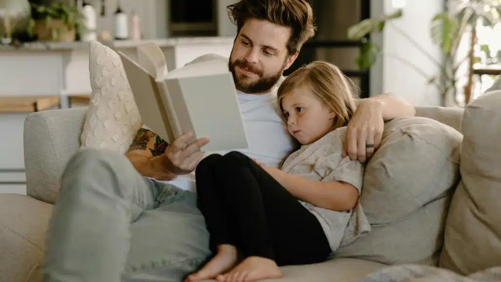 A father reading a book to his daughter on a couch.