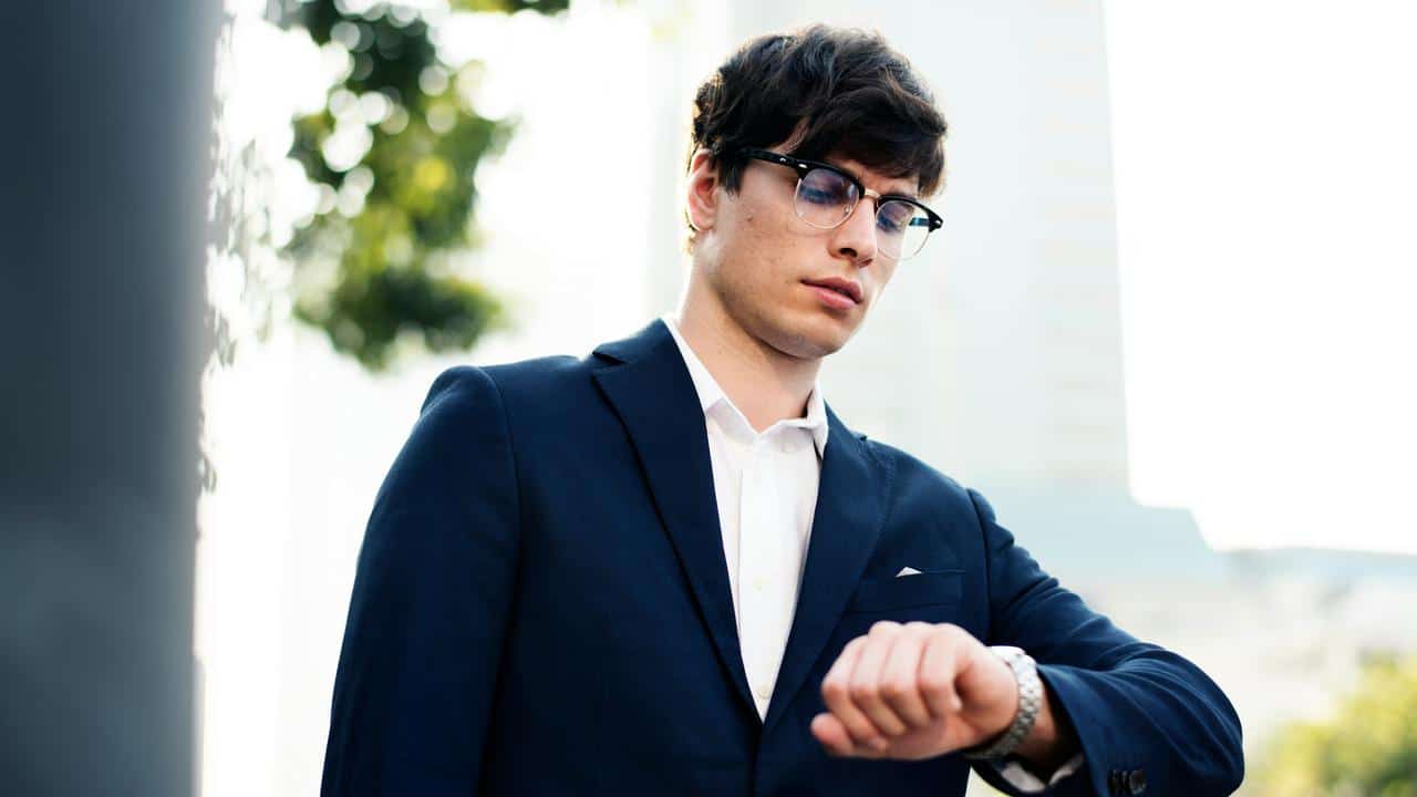 A man in a suit checking his wristwatch outdoors.