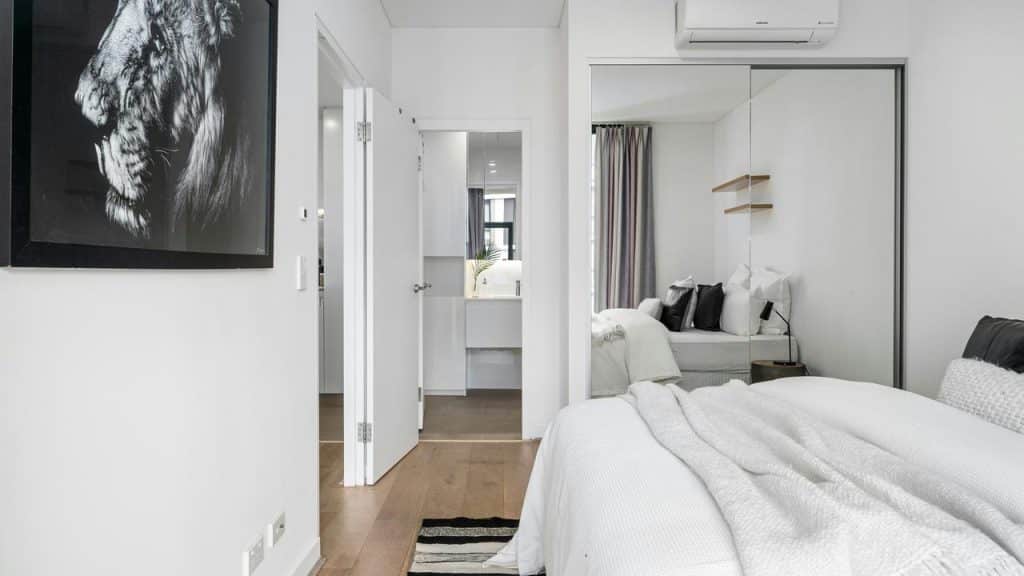 A white bedroom with a bed, mirrored closet, and a lion portrait.