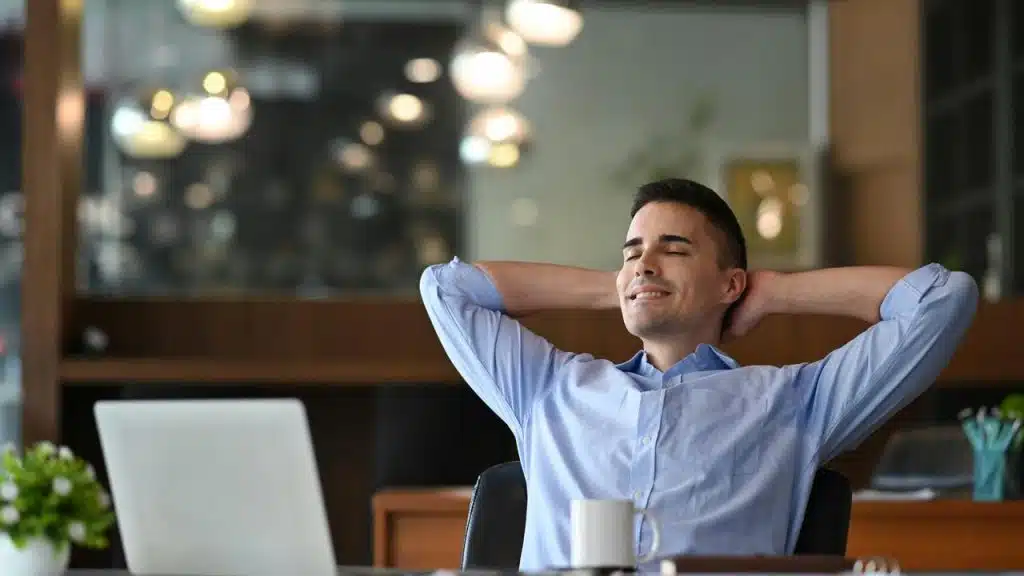 A man reclining in an office chair with a laptop and coffee mug.