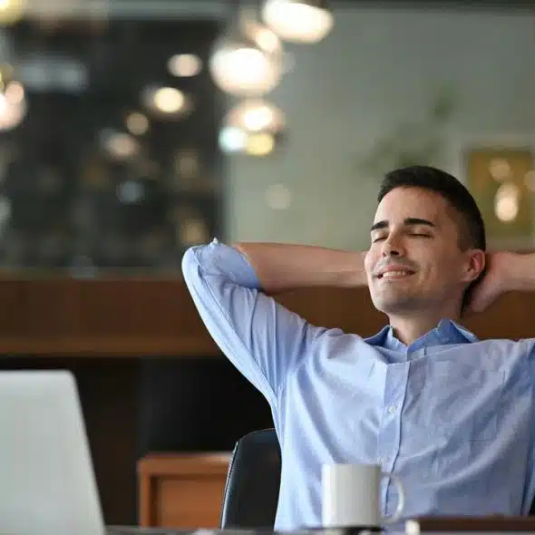 A man reclining in an office chair with a laptop and coffee mug.