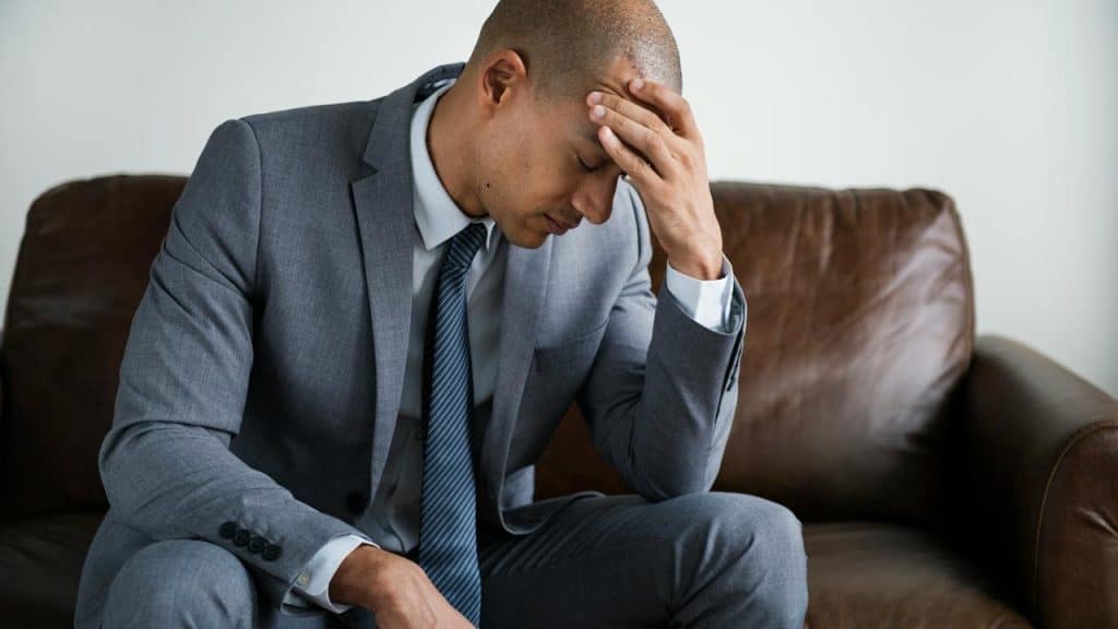 A man in a suit sitting on a couch with his head in his hand.