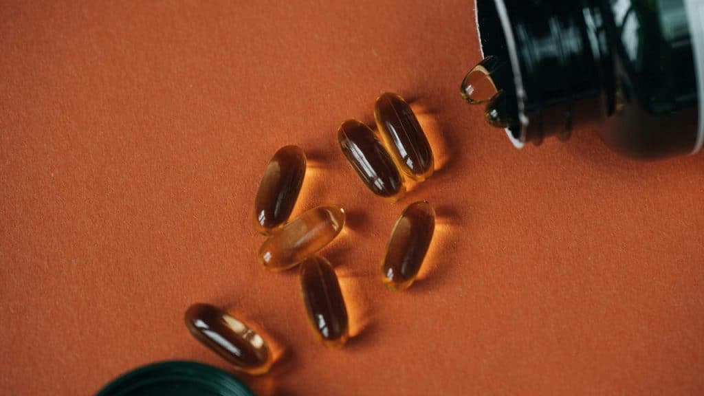 A cluster of amber gel capsules spilled from a bottle on an orange surface.