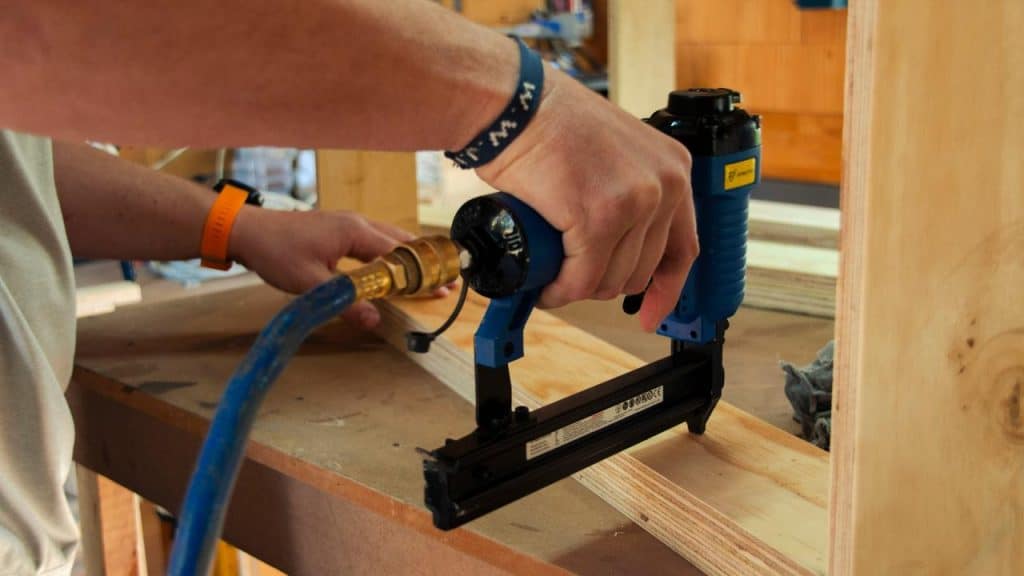 A person using a blue pneumatic nail gun on a wooden board.