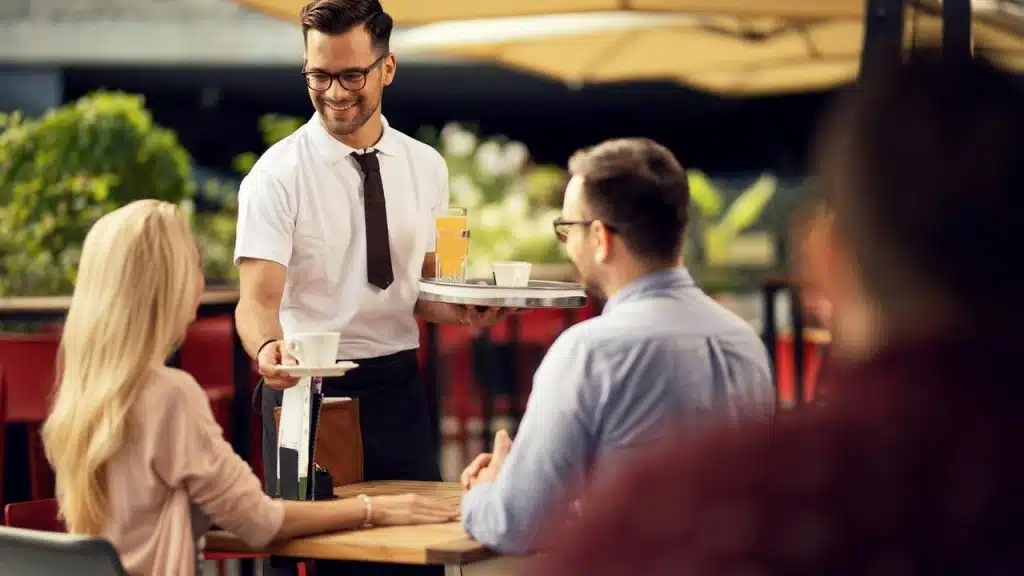 A waiter serving coffee and orange juice to a couple at an outdoor café.