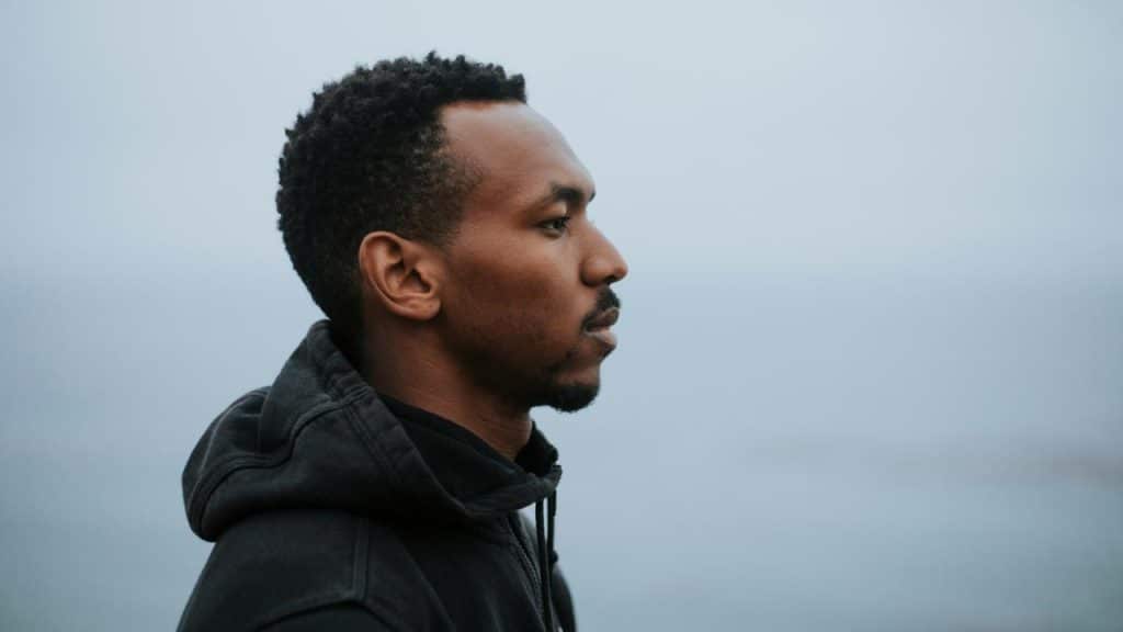 A man in a hoodie looking out over calm water.