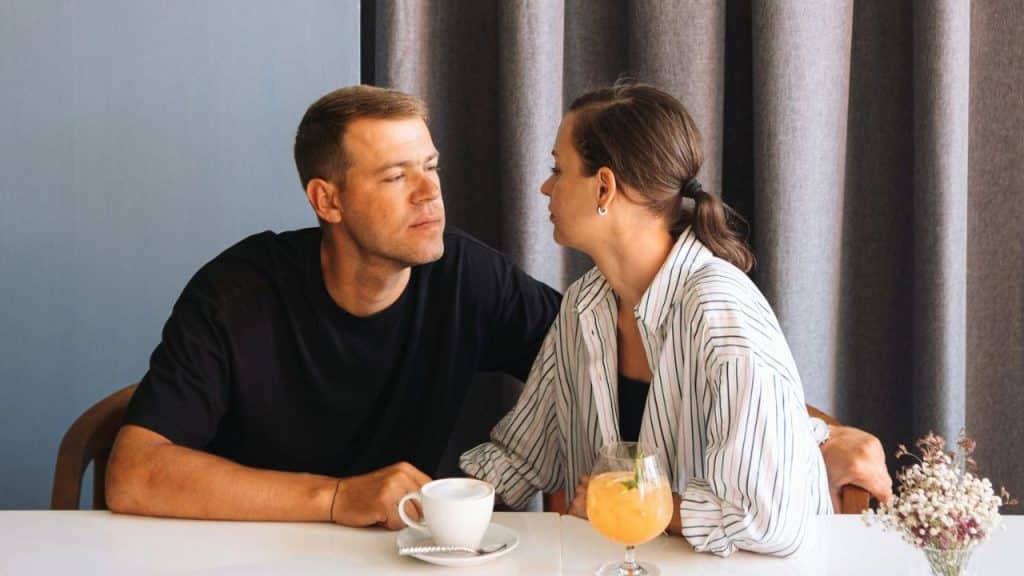 A man and a woman look at each other across a table with drinks.