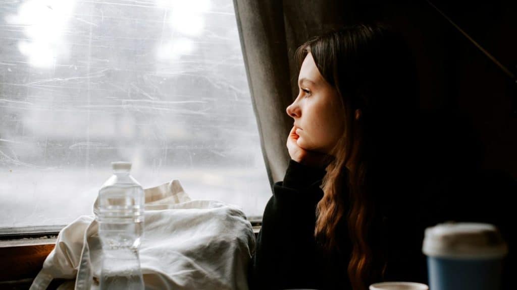A woman with long dark hair gazes out a window, resting her chin on her hand.