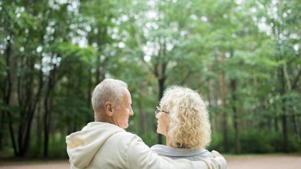 An older couple hugging in a forest.