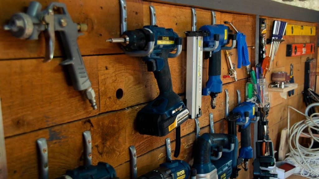 A wooden wall rack holding blue power drills, nail guns, and other hanging tools.
