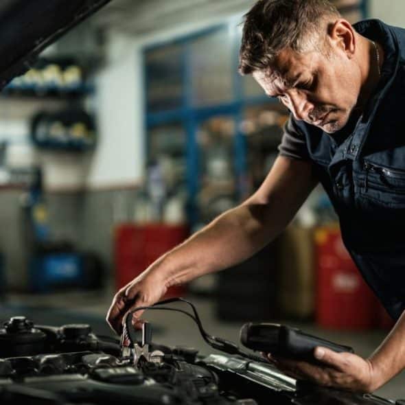 A mechanic in a gray shirt and dark blue vest works on a car engine.