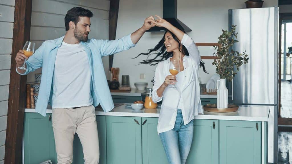 A couple dancing in a kitchen holding glasses of juice.