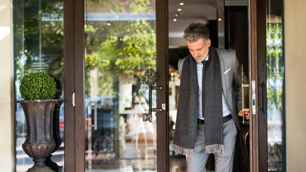 A man in a suit and scarf stepping through a glass door.