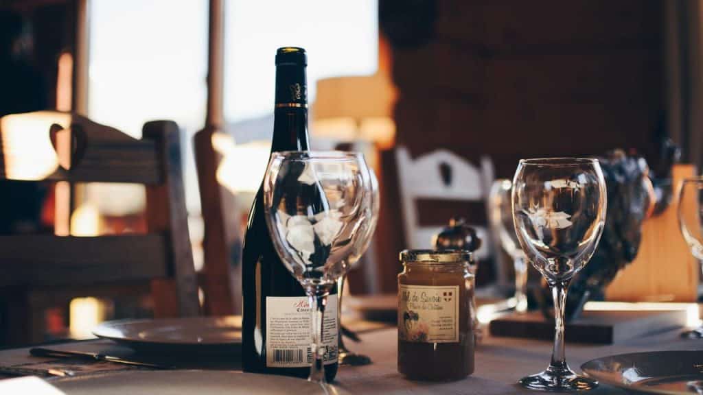 A wine bottle with glasses and a jar of honey on a table.