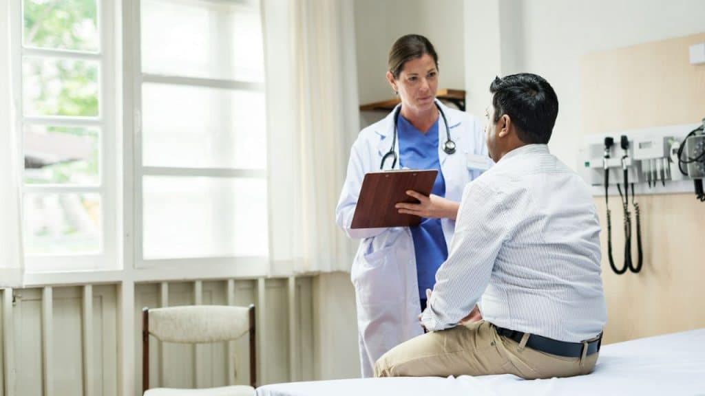 A nurse in blue gloves takes a man's blood in a bright room.