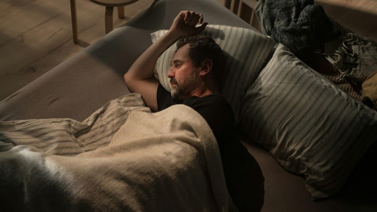 A man lies asleep in bed, with his arm above his head.