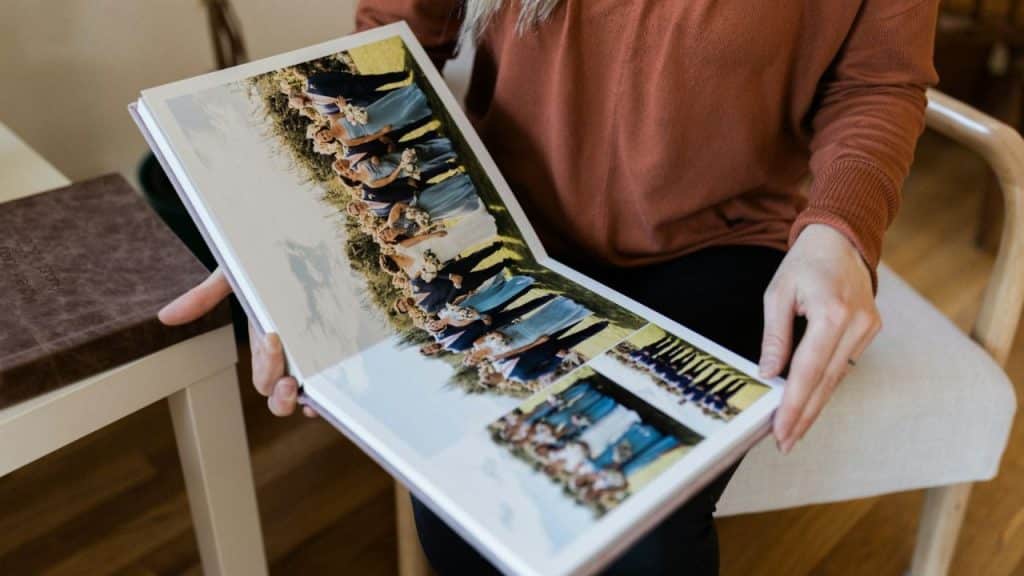 A woman in an orange shirt sits holding an open photo album.