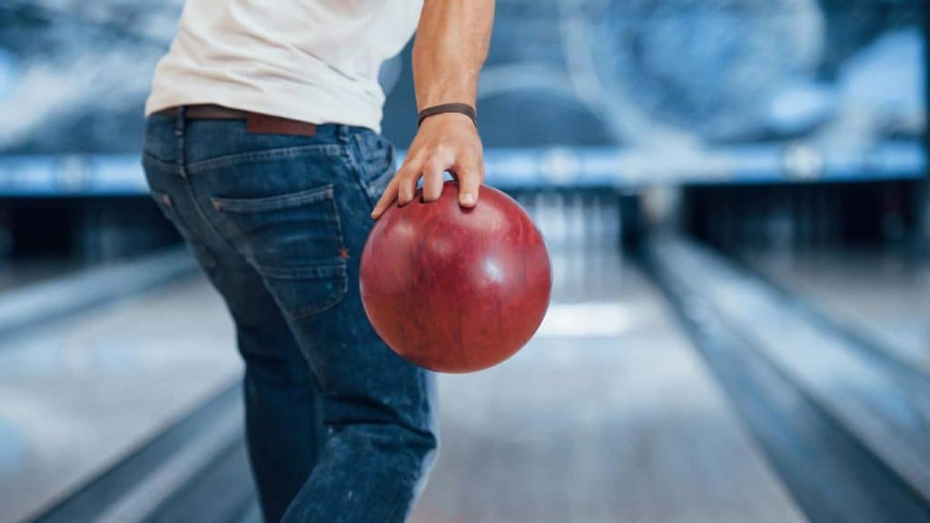 A bowler holding a red bowling ball at a lane.