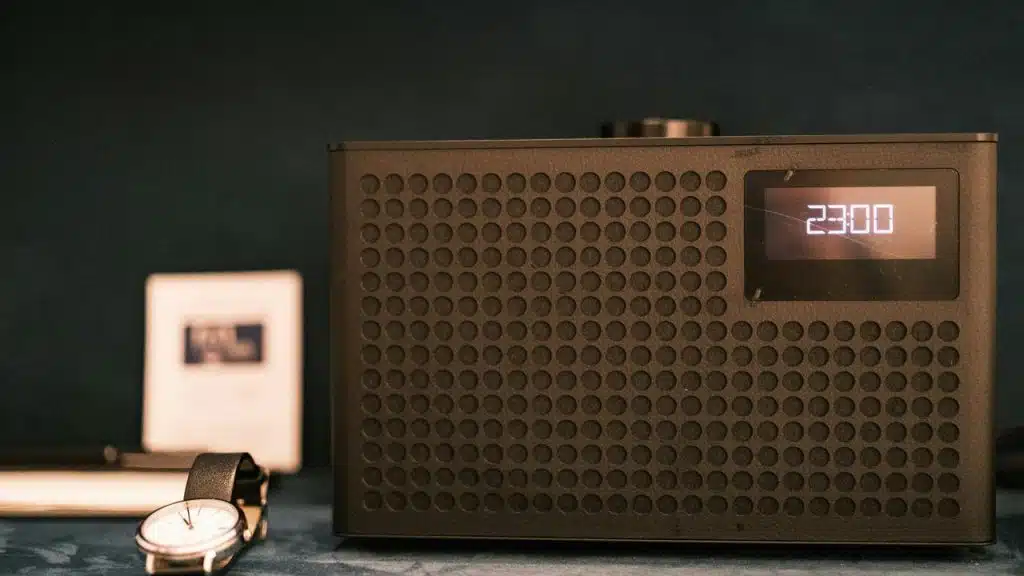 A black clock-radio displaying “23:00” beside a wristwatch.